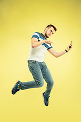 Image showing Full length portrait of happy jumping man with gadgets on yellow background