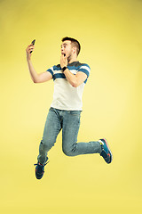 Image showing Full length portrait of happy jumping man with gadgets on yellow background