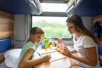 Image showing Mom and daughter sit at the table in the train and solve the puzzle in the children\'s magazine