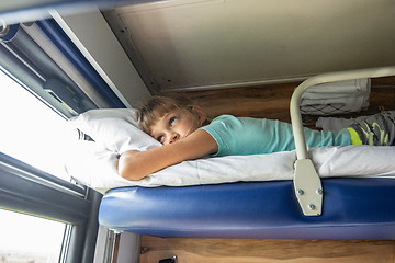 Image showing An eight-year-old girl lies on the top shelf of a reserved seat car and looks tiredly out the window