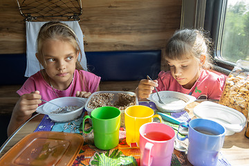 Image showing Two girls eat buckwheat with milk from plastic disposable tableware on a train