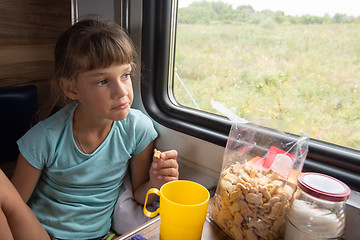 Image showing The girl eats cookies on the train and looks out the window