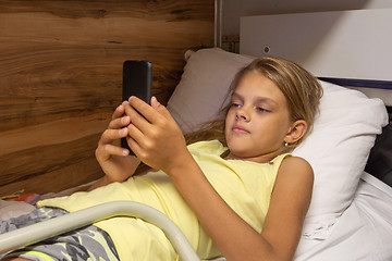 Image showing The girl lies on the top shelf in the carriage and plays in the smartphone
