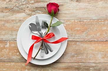 Image showing red rose on set of dishes with cutlery on table