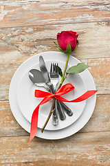 Image showing red rose on set of dishes with cutlery on table