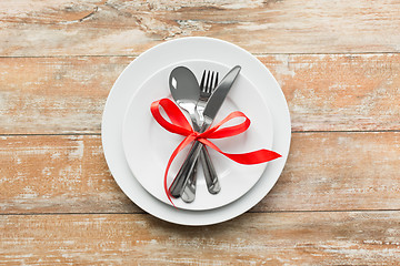 Image showing cutlery tied with red ribbon on set of plates