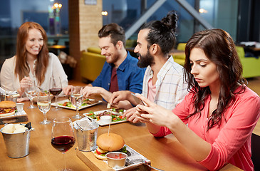 Image showing bored woman messaging on smartphone at restaurant