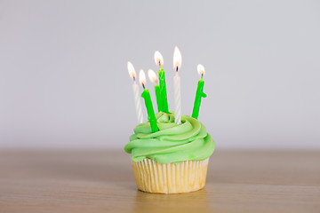 Image showing green cupcake with six burning candles on table