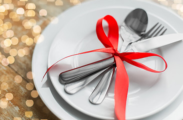 Image showing close up of cutlery tied with red ribbon on plates