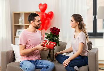 Image showing happy man giving woman flowers and present at home