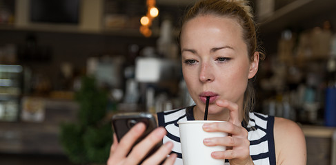 Image showing Thoughtful woman reading news on mobile phone while sipping coffee in coffee shop.