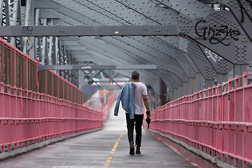 Image showing Rear view of unrecognizable stylish young man carrying jeans jacket over his shoulder walking on Williamsburg Bridge, Brooklyn, New York City.