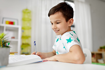 Image showing student boy with book writing to notebook at home