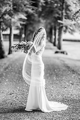 Image showing Full length portrait of beautiful sensual young blond bride in long white wedding dress and veil, holding bouquet outdoors in natural background.