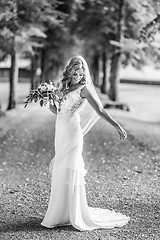 Image showing Full length portrait of beautiful sensual young blond bride in long white wedding dress and veil, holding bouquet outdoors in natural background.