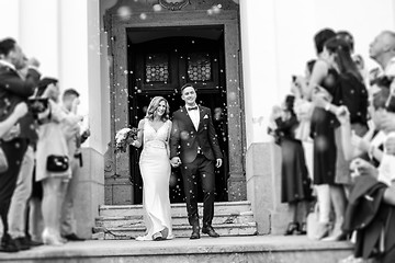 Image showing Newlyweds exiting the church after the wedding ceremony, family and friends celebrating their love with the shower of soap bubbles, custom undermining traditional rice bath