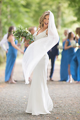 Image showing Full length portrait of beautiful sensual young blond bride in long white wedding dress and veil, holding bouquet outdoors in natural background