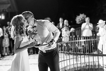 Image showing Happy bride and groom getting messy eating piece of wedding cake by their hands after cutting it.