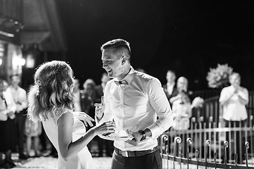 Image showing Happy bride and groom getting messy eating piece of wedding cake by their hands after cutting it.