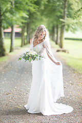 Image showing Full length portrait of beautiful sensual young blond bride in long white wedding dress and veil, holding bouquet outdoors in natural background