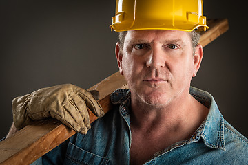 Image showing Serious Contractor in Hard Hat Holding Plank of Wood With Dramat