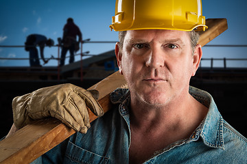 Image showing Serious Contractor in Hard Hat Carrying Wood Plank At Constructi