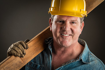 Image showing Smiling Contractor in Hard Hat Holding Plank of Wood With Dramat