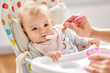 Image showing father feeding baby sitting in highchair at home