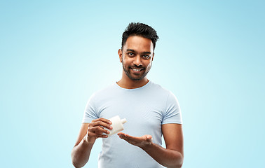 Image showing happy indian man applying lotion to his hand