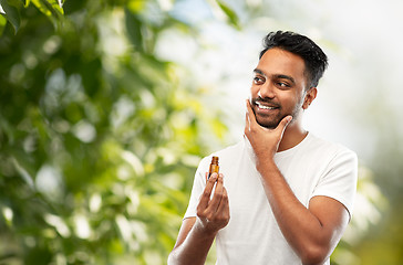 Image showing smiling indian man applying grooming oil to beard