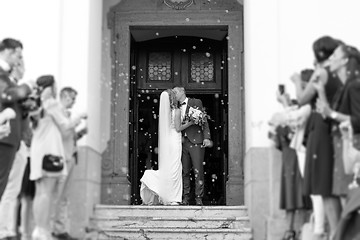 Image showing Newlyweds kissing while exiting the church after wedding ceremony, family and friends celebrating their love with the shower of soap bubbles, custom undermining traditional rice bath