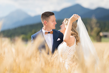 Image showing Groom hugs bride tenderly while wind blows her veil in wheat field somewhere in Slovenian countryside.