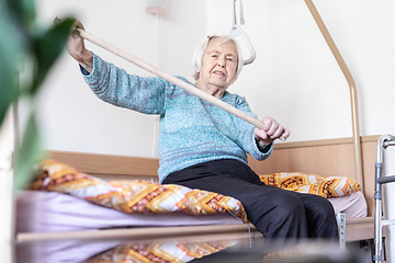 Image showing Elderly 96 years old woman exercising with a stick sitting on her bad.