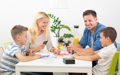 Image showing Happy young family playing card game at dining table at bright modern home.