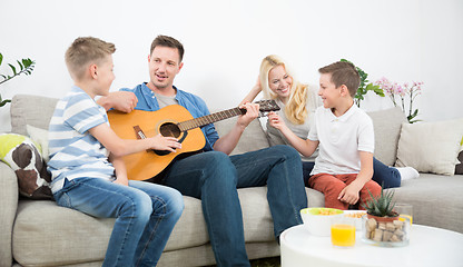Image showing Happy caucasian family smiling, playing guitar and singing songs together at cosy modern home