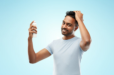 Image showing smiling indian man applying hair spray over blue