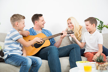 Image showing Happy caucasian family smiling, playing guitar and singing songs together at cosy modern home