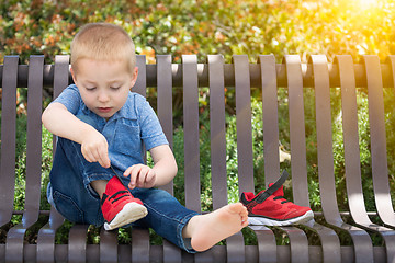 Image showing Young Boy Sitting On A Bench Putting On His Shoes At The Park