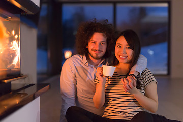Image showing happy multiethnic couple sitting in front of fireplace