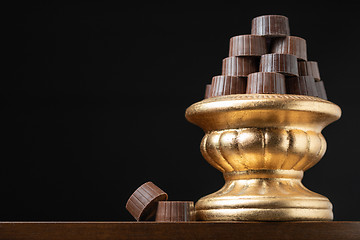 Image showing Stack of Fine Chocolates On Golden Pillar Dish With Dark Backgro