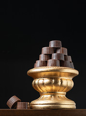 Image showing Stack of Fine Chocolates On Golden Pillar Dish With Dark Backgro