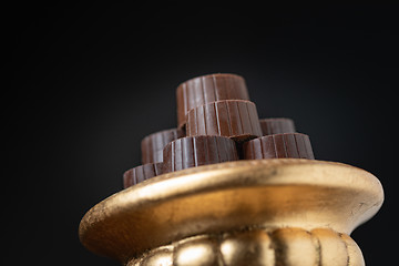 Image showing Stack of Fine Chocolates On Golden Pillar Dish With Dark Backgro