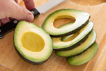 Image showing Male Hand Prepares Fresh Cut Avocado on Wooden Cutting Board