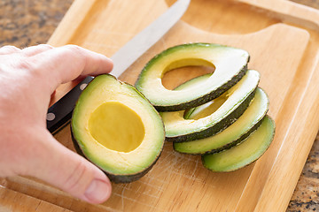 Image showing Male Hand Prepares Fresh Cut Avocado on Wooden Cutting Board