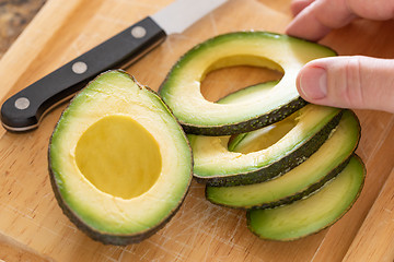 Image showing Male Hand Prepares Fresh Cut Avocado on Wooden Cutting Board