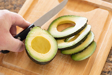 Image showing Male Hand Prepares Fresh Cut Avocado on Wooden Cutting Board