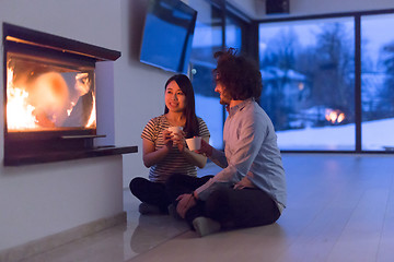 Image showing happy multiethnic couple sitting in front of fireplace