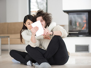 Image showing multiethnic couple using tablet computer in front of fireplace