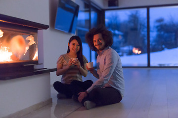 Image showing happy multiethnic couple sitting in front of fireplace