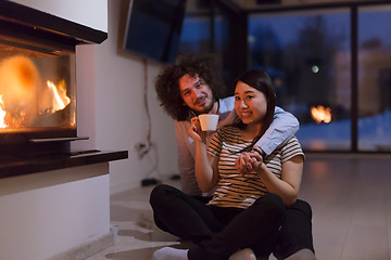 Image showing happy multiethnic couple sitting in front of fireplace